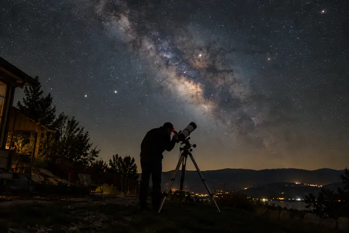 A person looking through a backyard telescope under a starry sky.