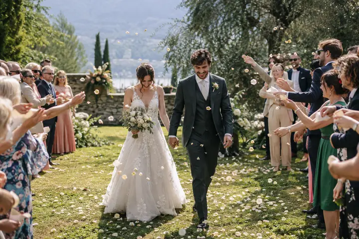 A bride and groom walking hand in hand as guests toss petals.