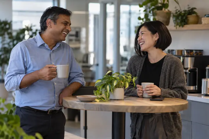 Two coworkers chatting over coffee in an office kitchen.